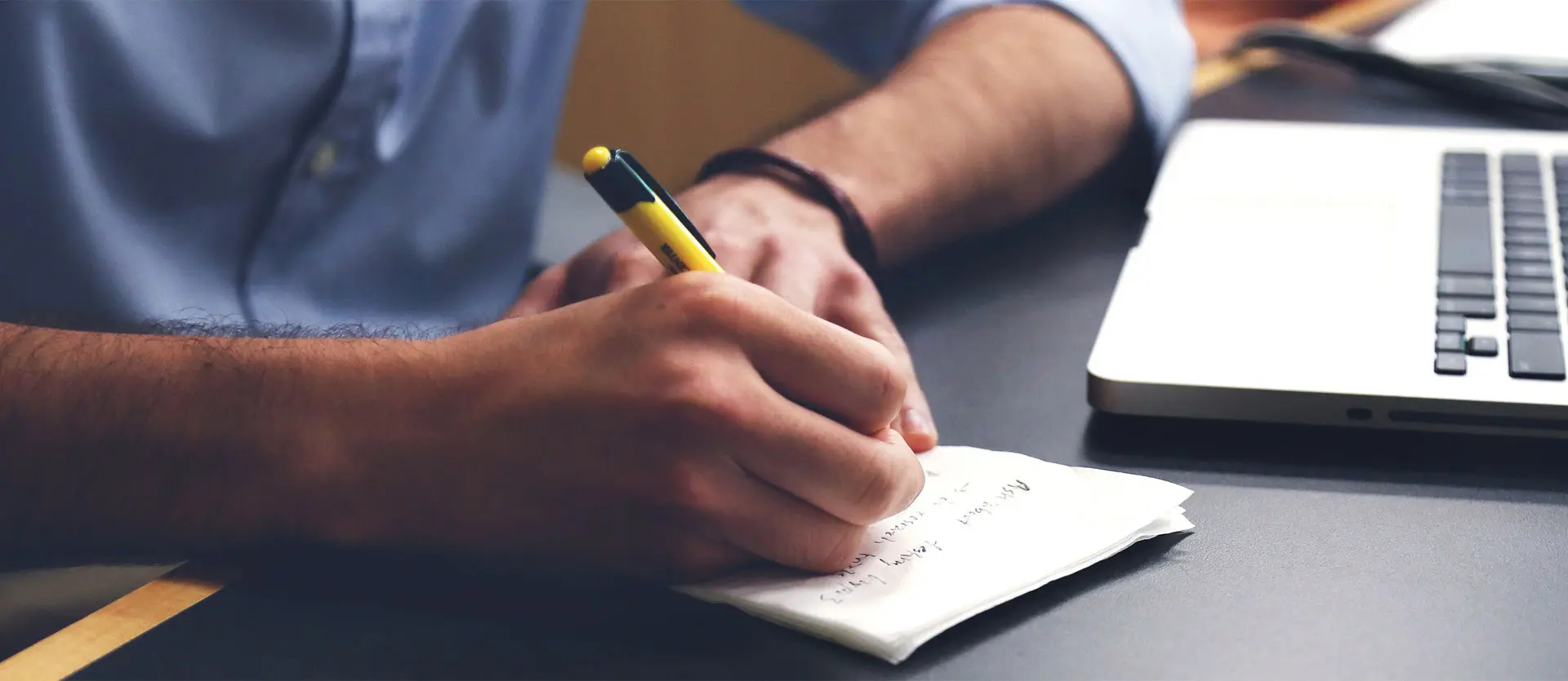 Man infront of laptop writing on a desk with paper